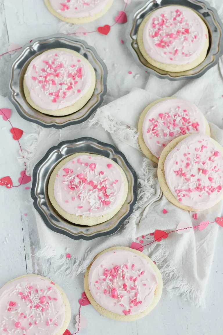 Biscuits de couleur rose avec un fond blanc rempli de petit coeur et trois assiettes en métal