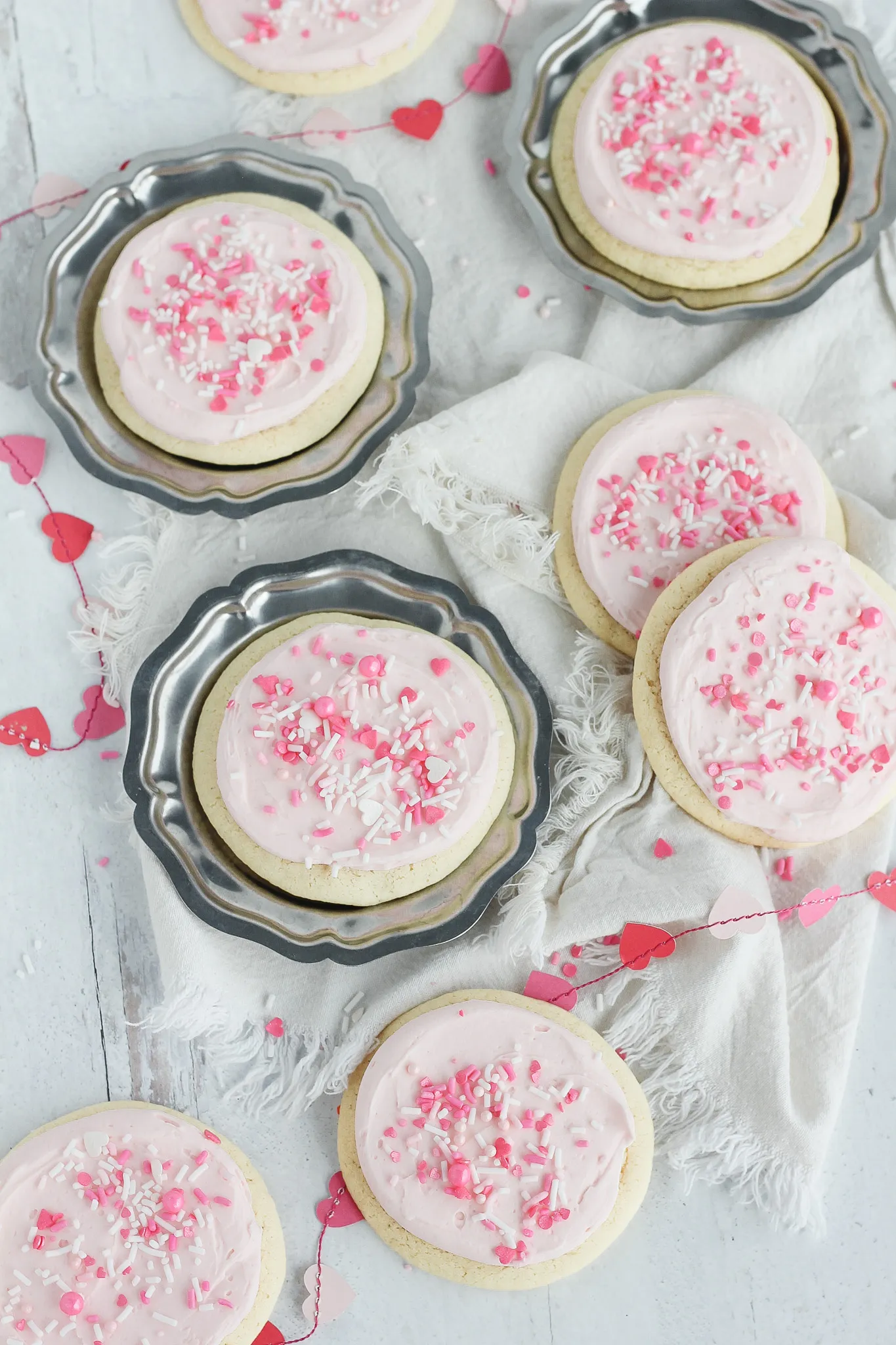 Biscuits de couleur rose avec un fond blanc rempli de petit coeur et trois assiettes en métal