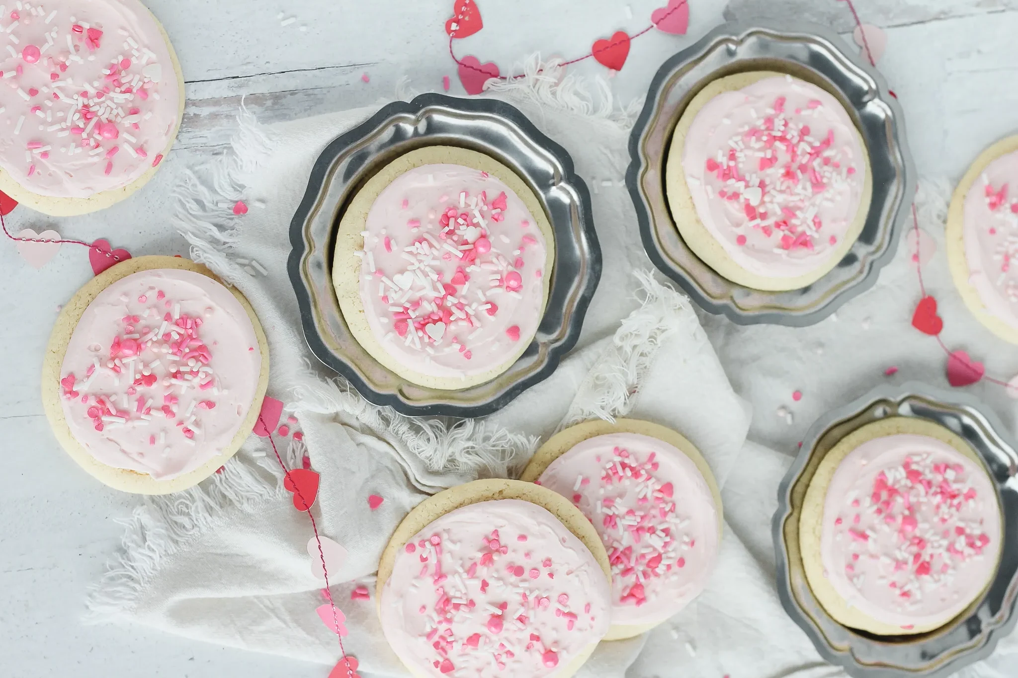 Biscuits de couleur rose avec un fond blanc rempli de petit coeur et trois assiettes en métal