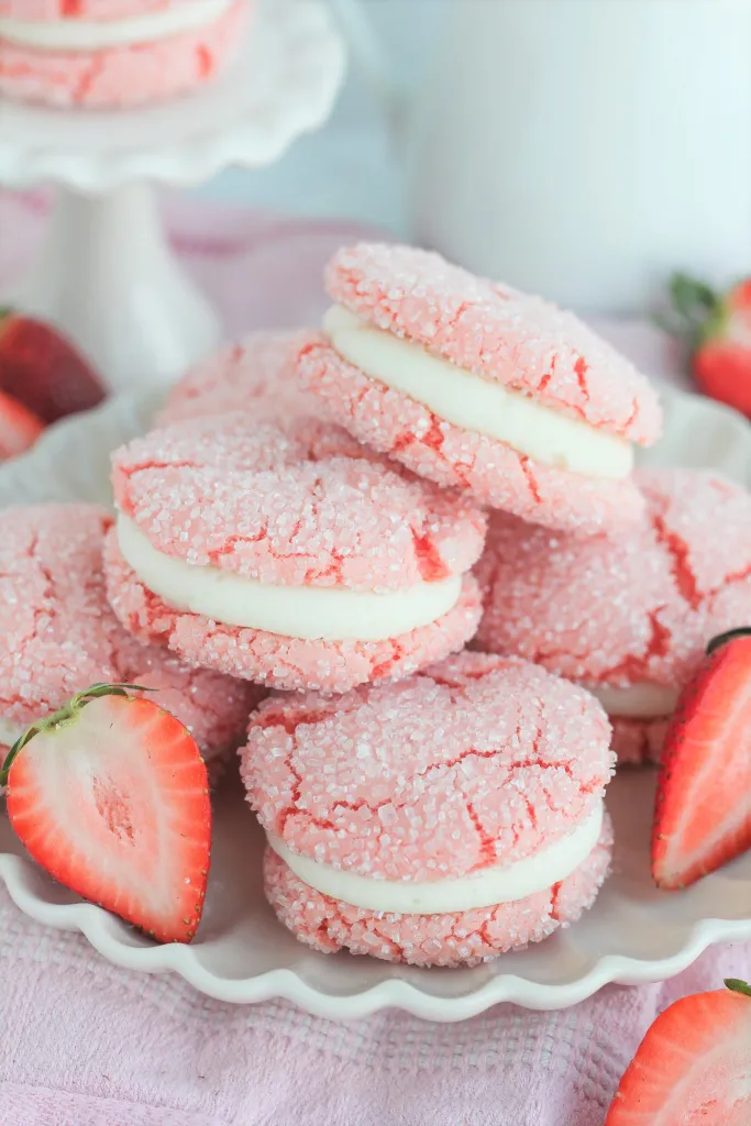 Macaron aux fraise de couleur rose sur une assiette blanche avec des fraises coupés en deux